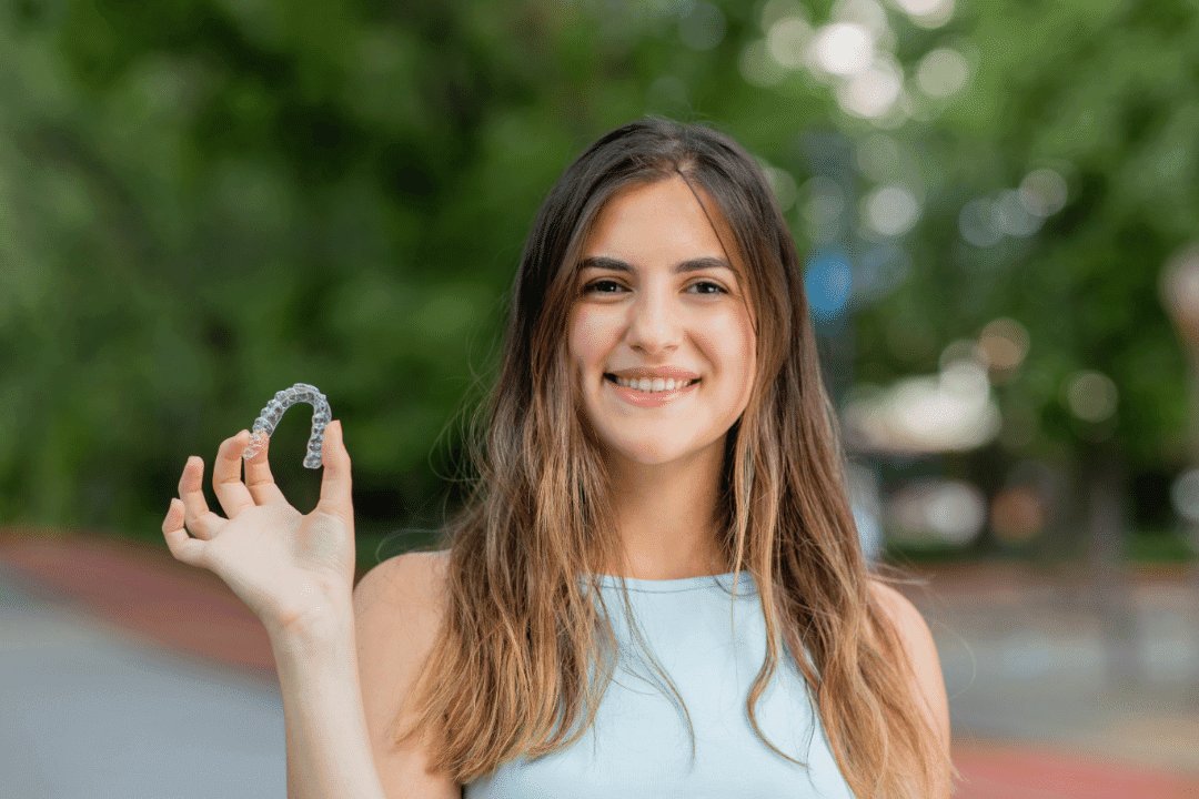 young woman holding night guard retainer outdoors smiling